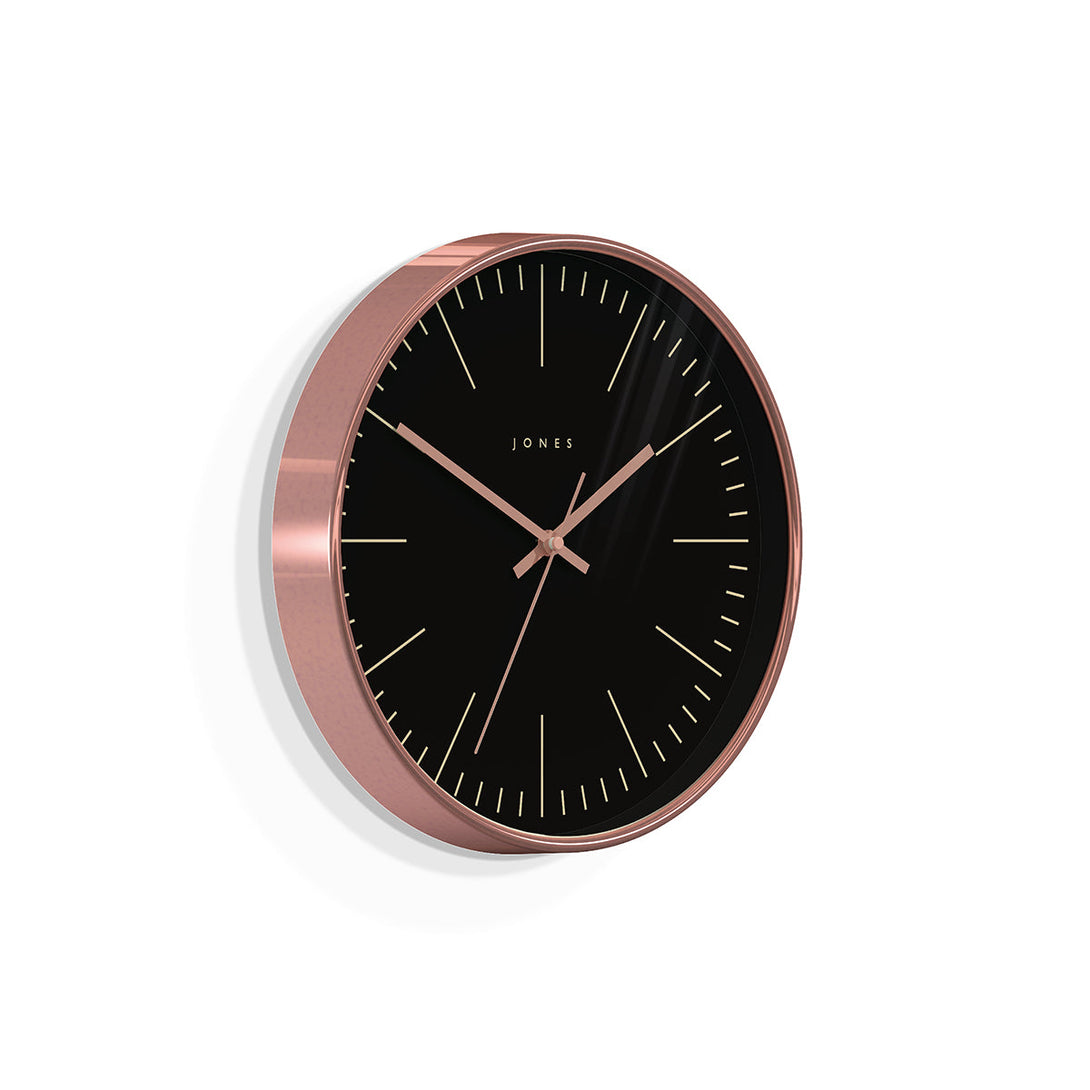 Skewed view of the modern Studio wall clock by Jones Clocks in a copper effect with a reverse black marker dial and copper hands