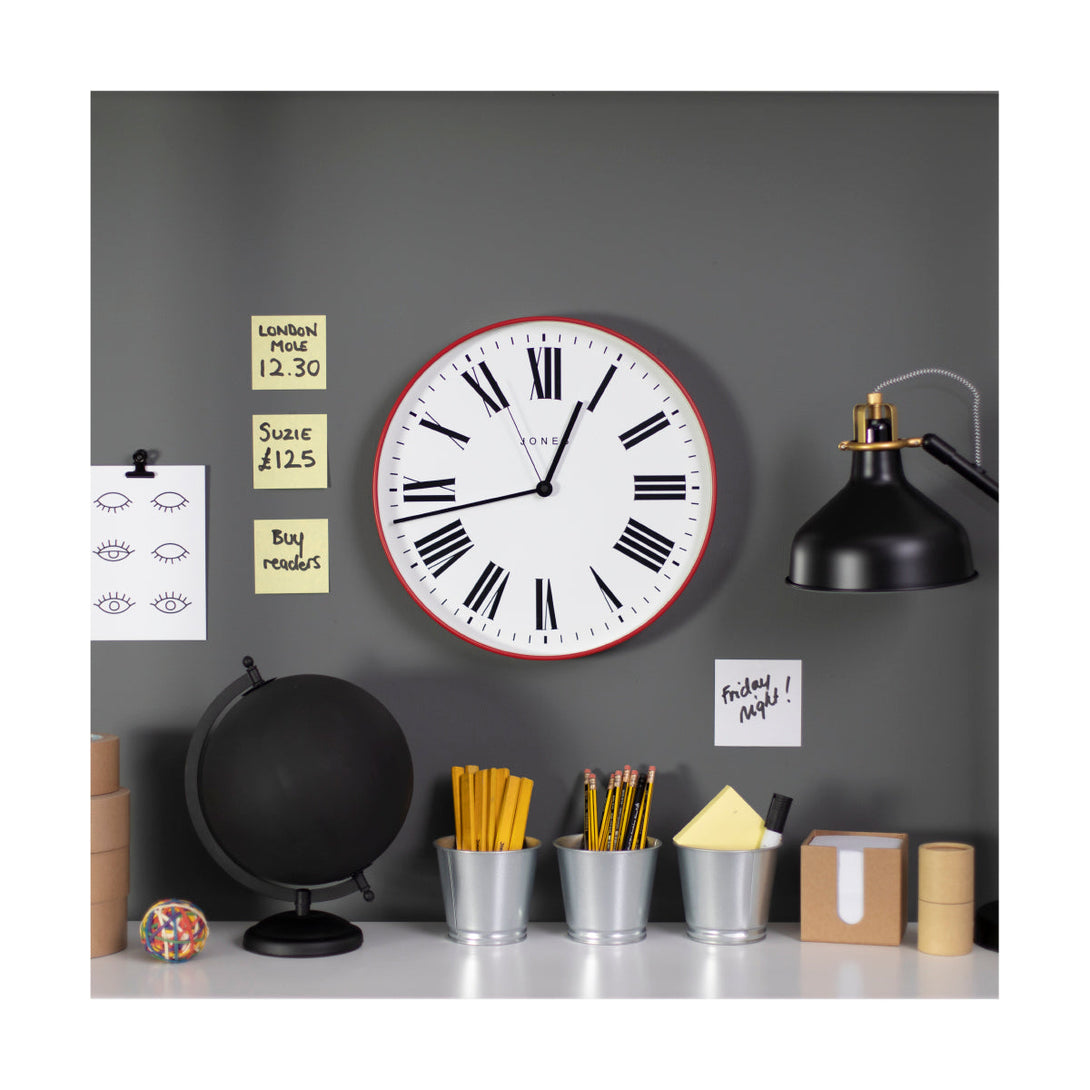 Magazine wall clock by Jones Clocks in a red case with a minimalist Roman numeral dial, in an office setting- JMAG444ER