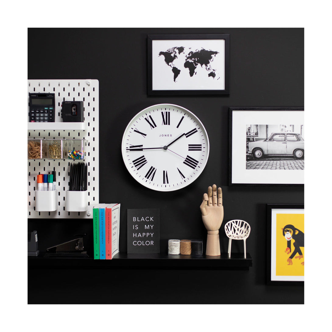 Magazine wall clock by Jones Clocks in a white case with a minimalist Roman numeral dial on a gallery wall - JMAG444W