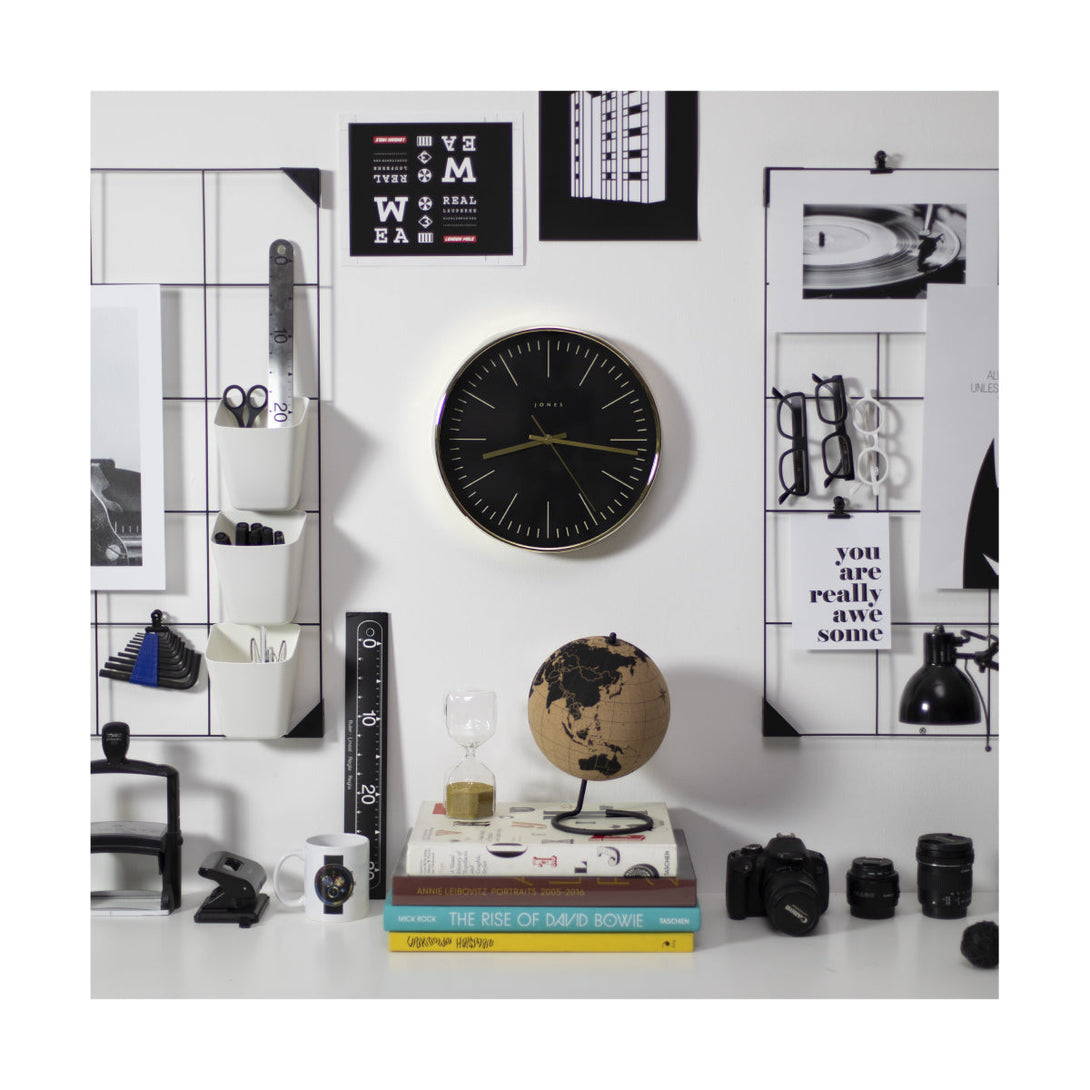 Studio wall clock in a gold effect by Jones Clocks with a reverse grey marker dial and straight metal hands on an office wall