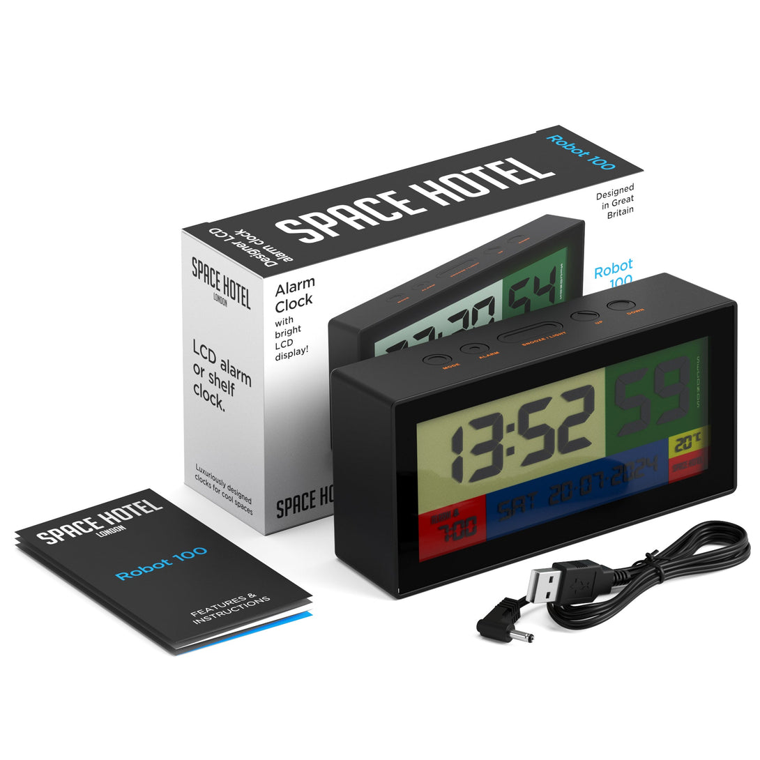 Skewed tilted view of the Space Hotel Robot 100 LCD alarm clock in black with multicoloured backlights, with packaging, instructions, and USB cable.